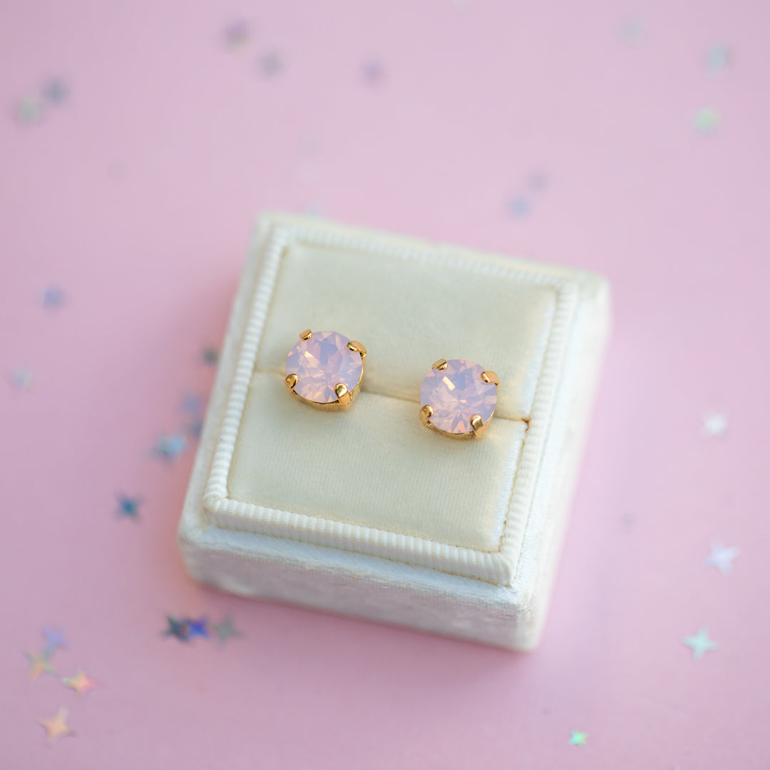 Pair of pink opal stud earrings in a white box on a pink background