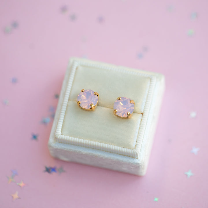 Pair of pink opal stud earrings in a white box on a pink background