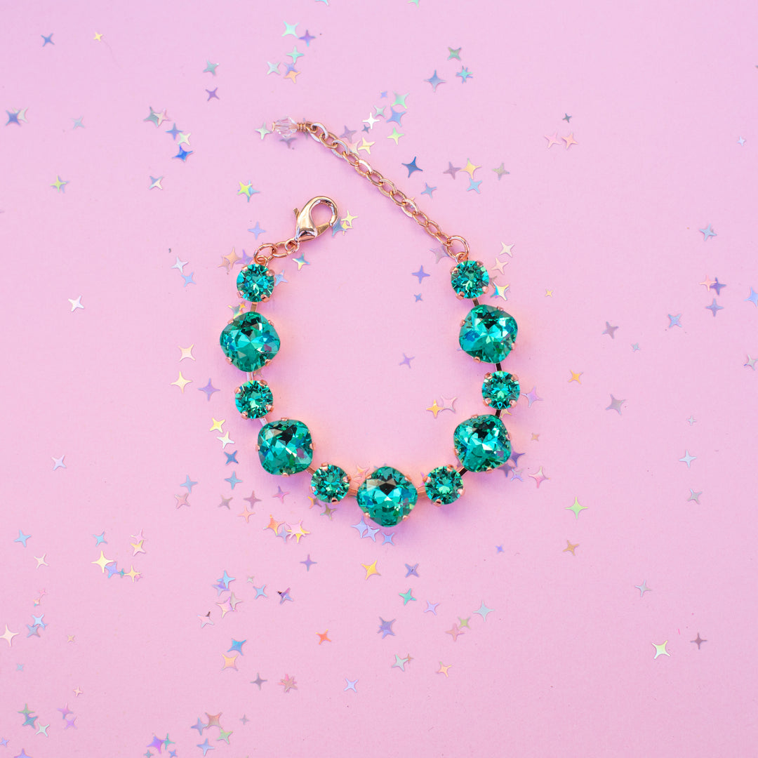 Teal gemstone bracelet on a pink background with star-shaped confetti