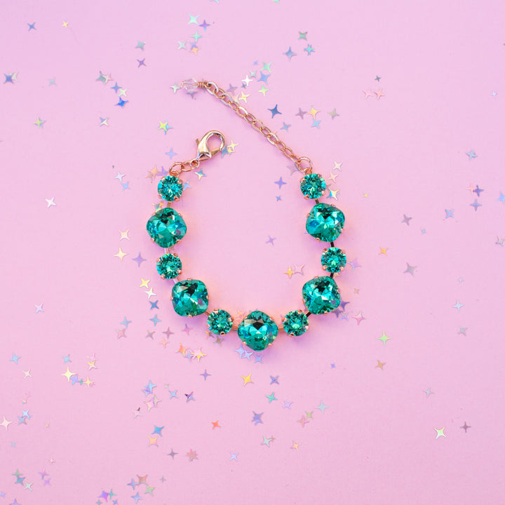Teal gemstone bracelet on a pink background with star-shaped confetti