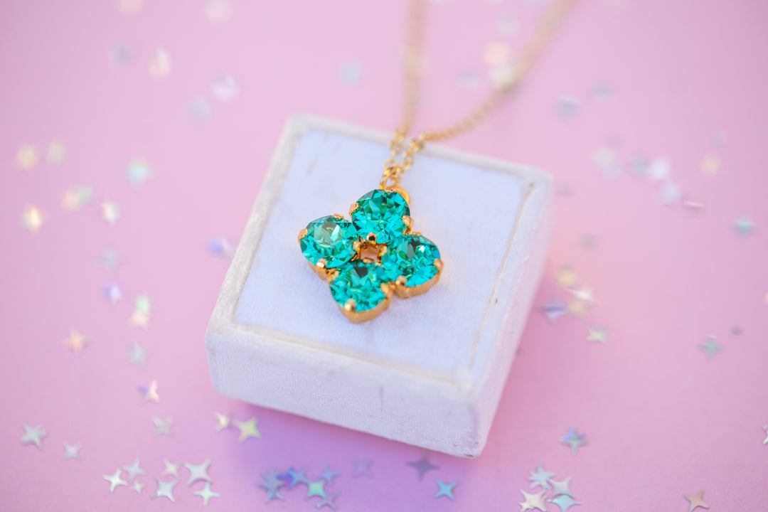 Necklace with a green flower pendant on a white box against a pink background with star confetti.