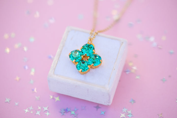 Necklace with a green flower pendant on a white box against a pink background with star confetti.