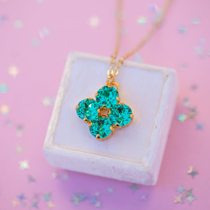Green floral pendant necklace on a white box with a pink background