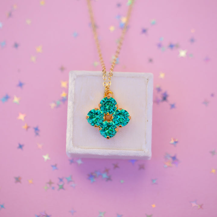 Turquoise flower-shaped necklace on a white stand against a pink background with confetti.