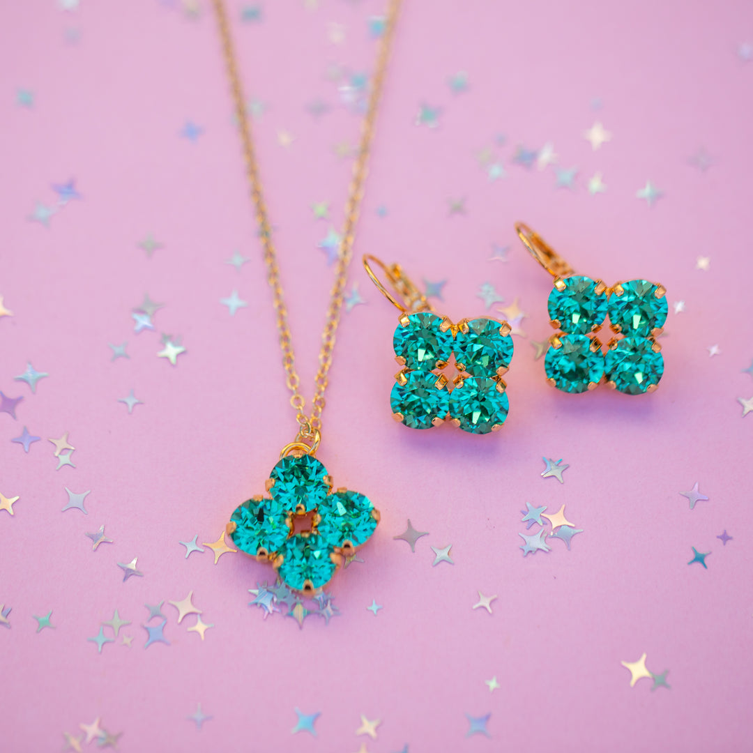 Teal flower-shaped jewelry set on a pink background with star confetti