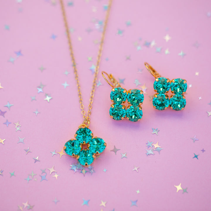 Teal flower-shaped jewelry set on a pink background with star confetti