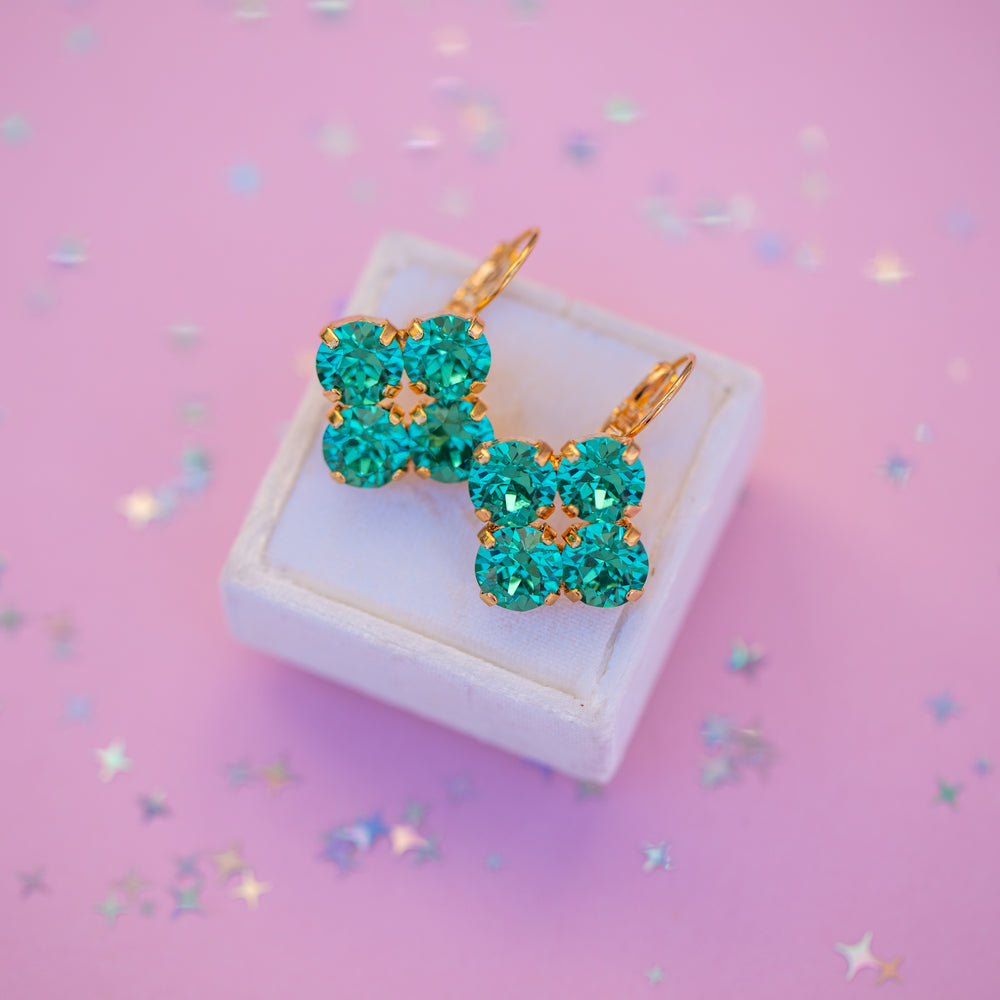 Pair of turquoise crystal earrings on a white box with a pink background
