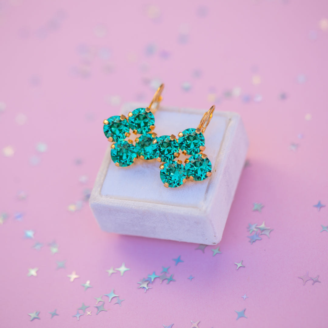 Turquoise bow-shaped earrings on a white box with a pink background