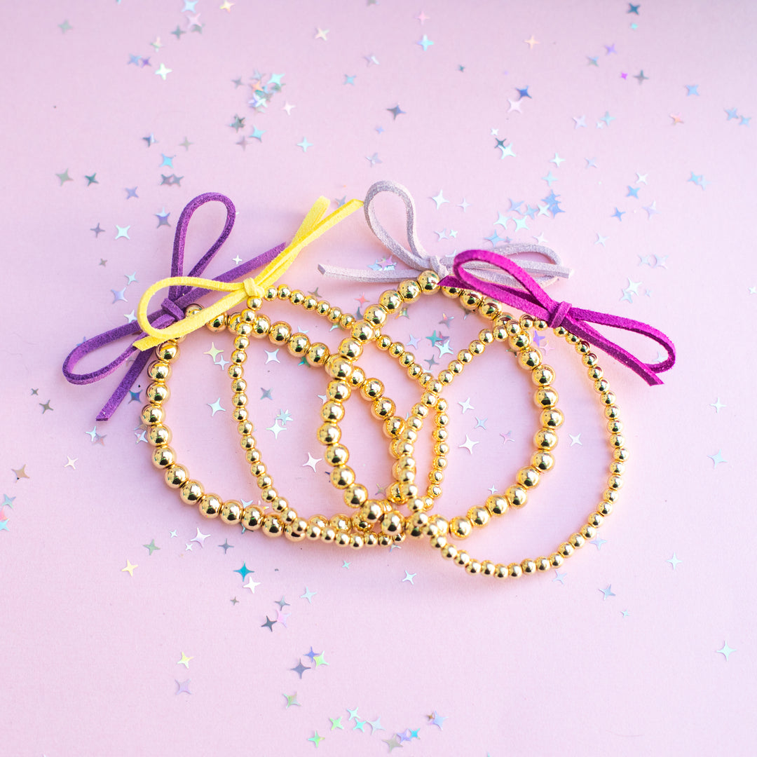 Gold beaded bracelets with colorful ribbons on a pink background