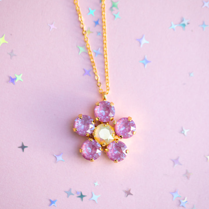 Necklace with a pink flower-shaped pendant on a pink background with star confetti
