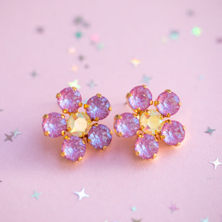Pink flower-shaped earrings on a pink background with star and cloud decorations